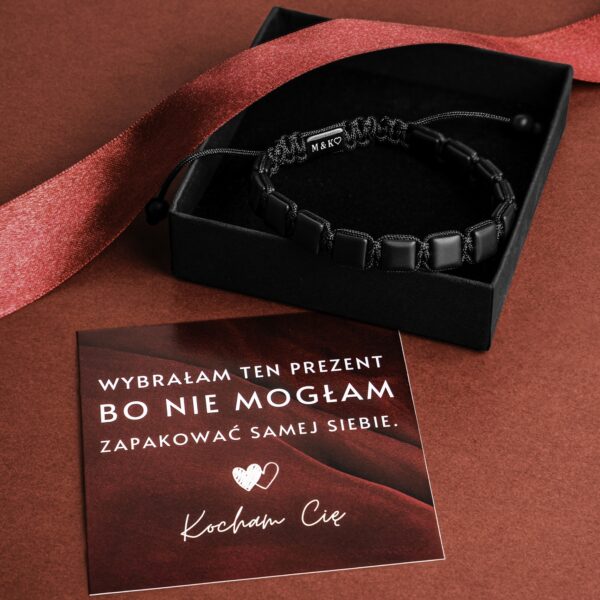 Czarna bransoletka w pudełku obok kartki z napisem 'Wybrałam ten prezent bo nie mogłam zapakować samej siebie. Kocham Cię'.
