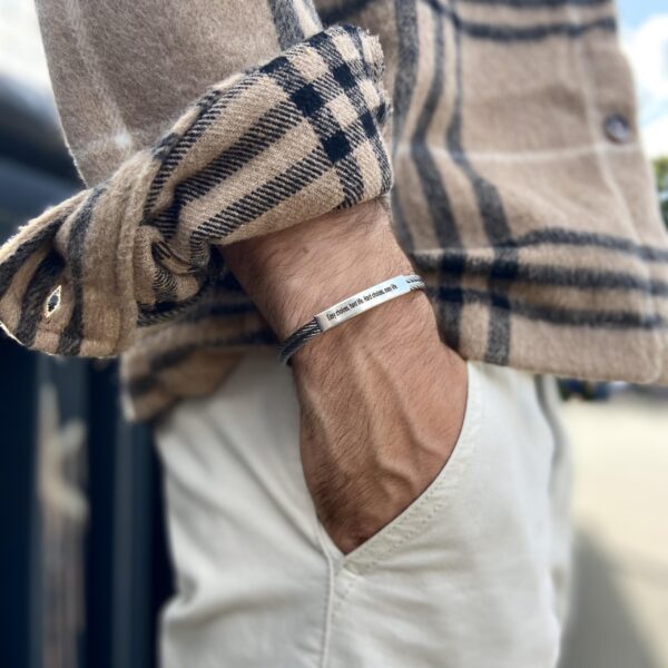 Osoba w koszuli w kratkę nosząca bransoletkę z napisem na nadgarstku.