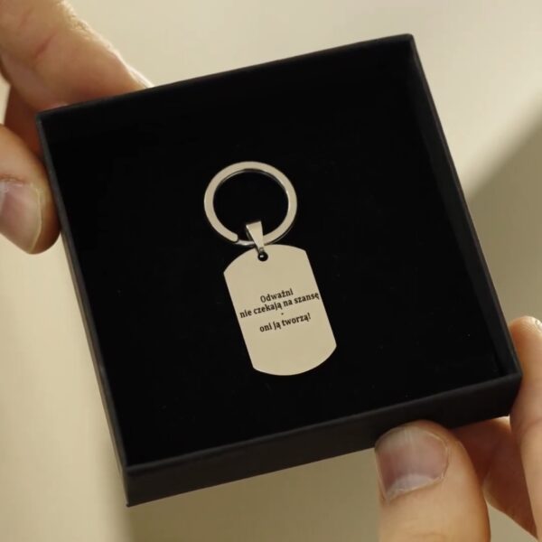 Brelok z cytatem: Odważni nie czekają na szansę, oni ją tworzą, umieszczony w czarnym pudełku.