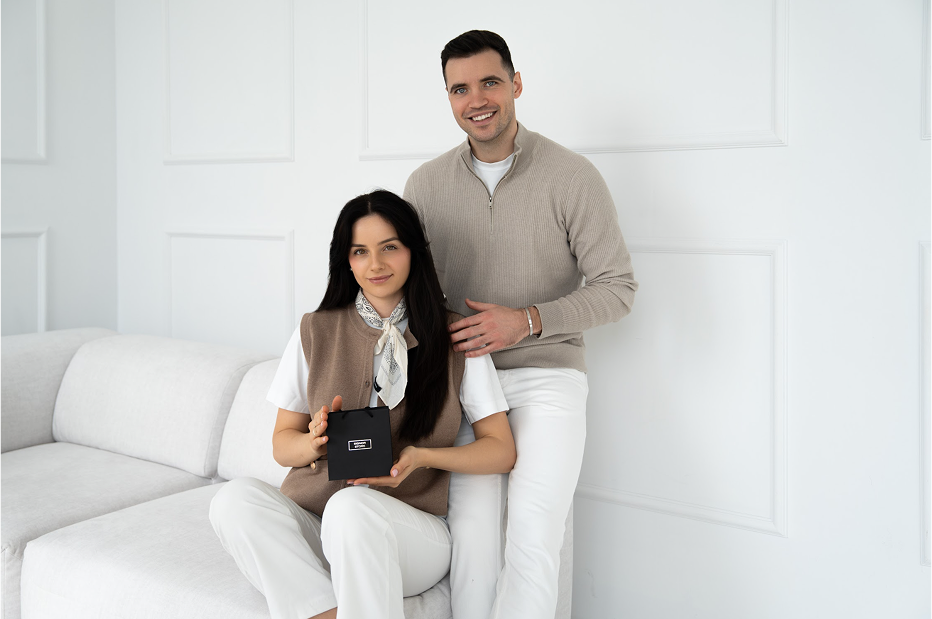 Kobieta siedząca na sofie trzyma pudełko, partner stoi obok niej.