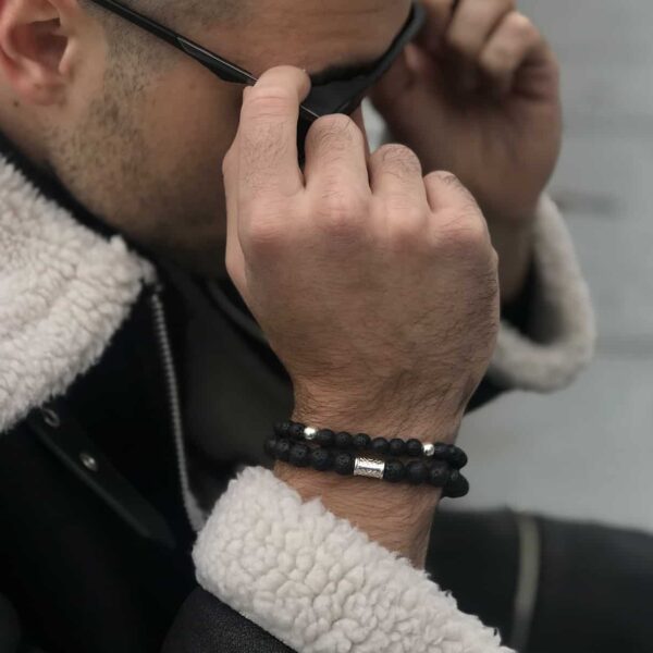 Mężczyzna poprawiający okulary przeciwsłoneczne z bransoletkami na nadgarstku.