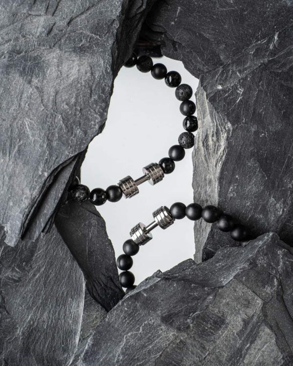 Bransoletka z czarnych koralików z metalowymi elementami otoczona łupkowymi skałami.