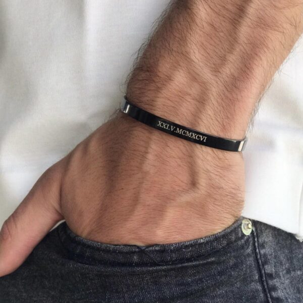 Męska ręka z czarną bransoletką z wygrawerowaną datą rzymską XXI.V.MCMXCVI.