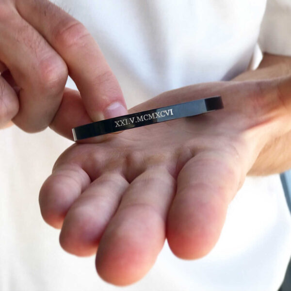 Osoba trzymająca metalową bransoletkę z grawerem w języku rzymskim.