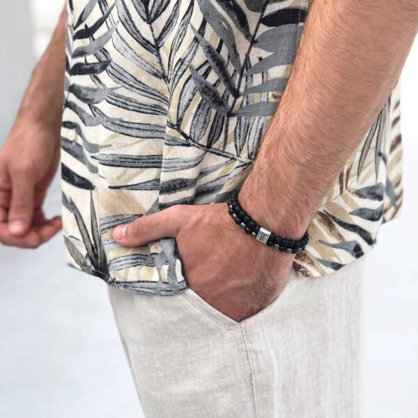 Mężczyzna w koszuli z deseniem roślinnym i bransoletką na nadgarstku.