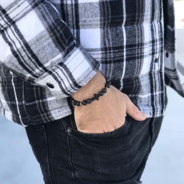 Osoba w kratkowanej koszuli z ręką w kieszeni, nosząca czarną bransoletkę.
