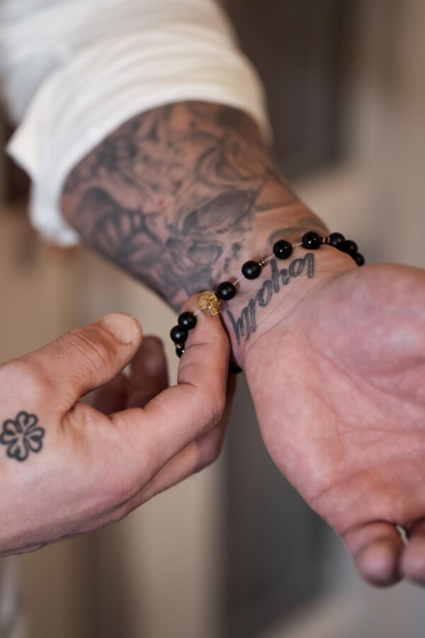 Zbliżenie na tatuaż na przedramieniu osoby, która zakłada bransoletkę z czarnych koralików.