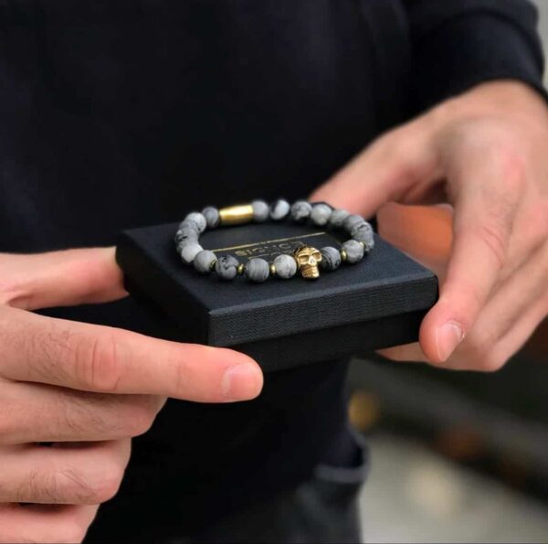 Osoba trzymająca pudełko z bransoletką z czaszką i koralikami.