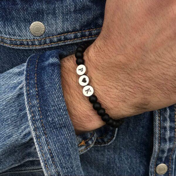 Bransoletka z czarnych koralików z literami P ♥ K na nadgarstku w dżinsowej kurtce.