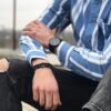 Mężczyzna w niebieskiej koszuli w paski z zegarkiem na ręku i bransoletką.