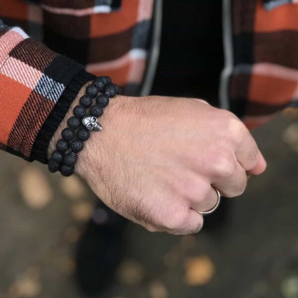 Ręka w kraciastej koszuli z czarną bransoletką i obrączką na palcu.