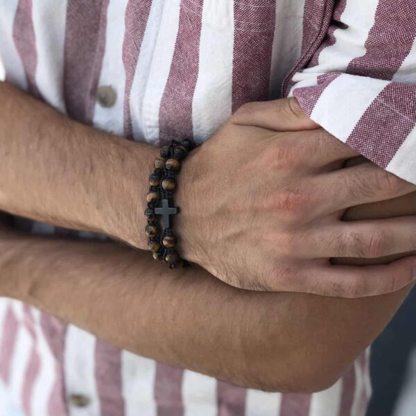 Mężczyzna w koszuli w paski z bransoletką z krzyżem na ręce.