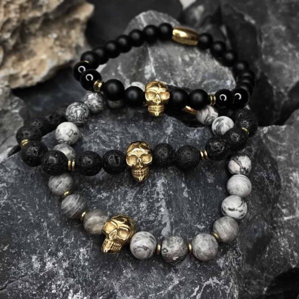 Trzy bransoletki z czaszkami na tle szarych kamieni.