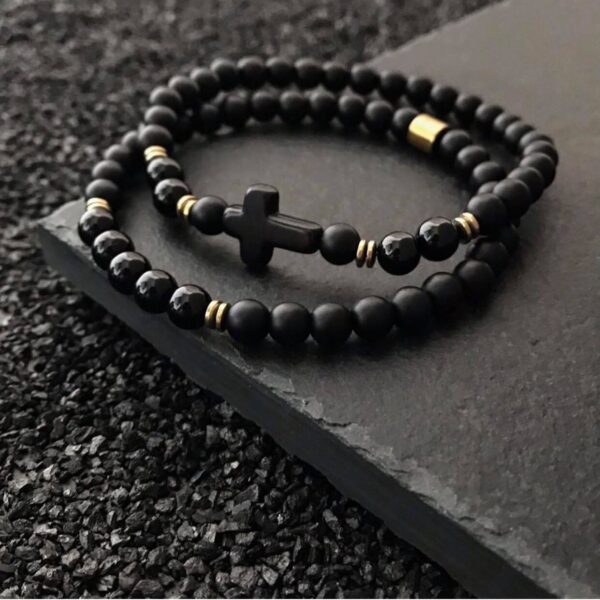 Czarne bransoletki z koralików i krzyżykiem, leżące na ciemnej powierzchni.