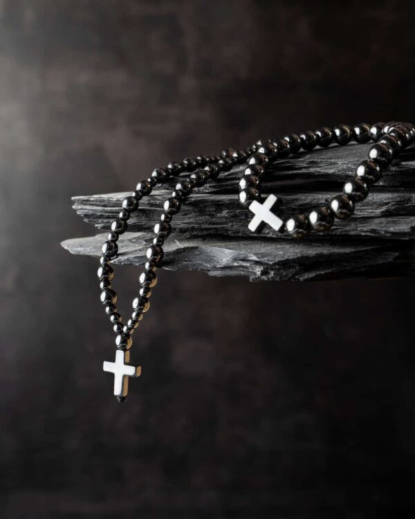 Czarne koraliki z krzyżem na tle ciemnego kamienia.
