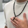 Osoba nosząca czarny różaniec z krzyżykiem na szyi.