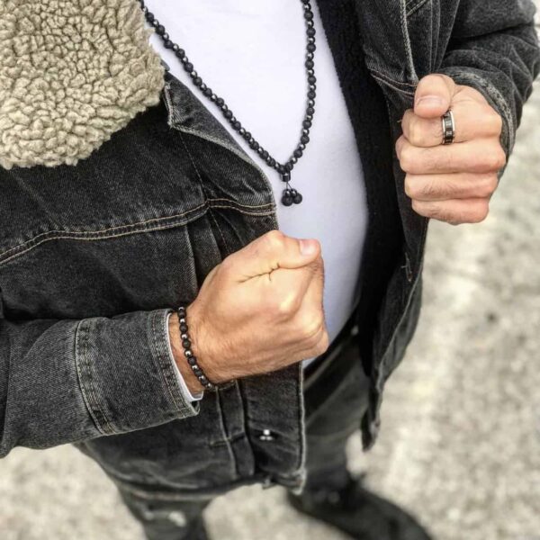 Osoba w kurtce dżinsowej, nosząca ciemny naszyjnik i bransoletkę, trzyma zaciśnięte pięści.