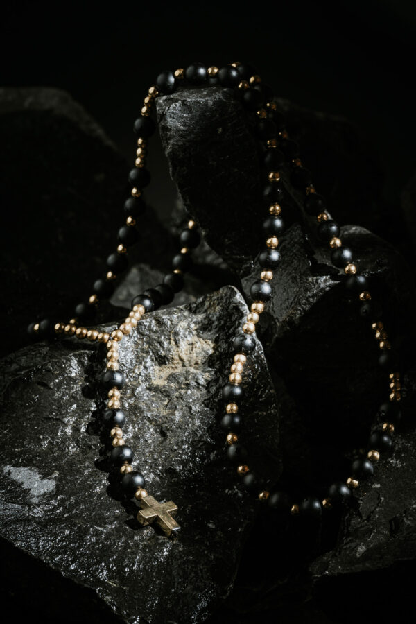 Czarny różaniec z złotymi koralikami na ciemnych kamieniach.