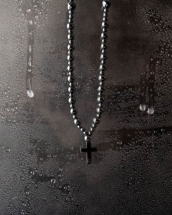Naszyjnik z czarnym krzyżem na mokrej powierzchni.