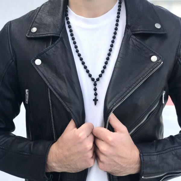 Osoba w czarnej skórzanej kurtce i białej koszulce nosi czarny różaniec z krzyżem.