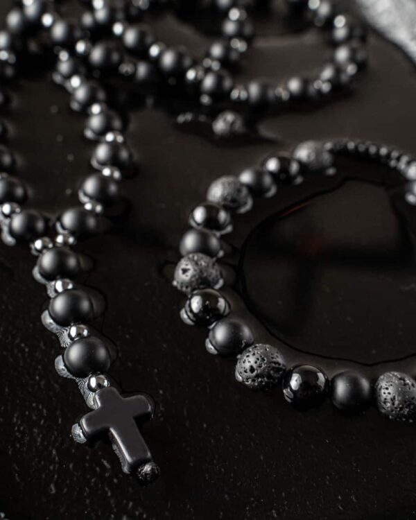 Bransoletka z czarnych koralików z krzyżykiem na czarnym tle.