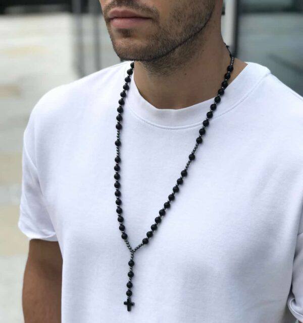 Mężczyzna w białej koszulce noszący czarny naszyjnik z krzyżykiem.