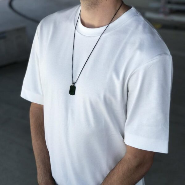 Osoba w białej koszulce z medalionem na szyi.