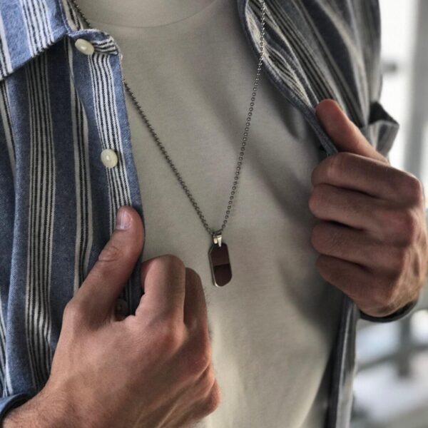 Mężczyzna w biały T-shirt i koszuli w paski, trzymający naszyjnik z zawieszką.