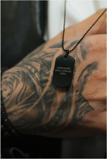 Dłoń z tatuażem trzymająca naszyjnik z napisem 'Wybieraj ludzi, którzy wybierają Ciebie'.