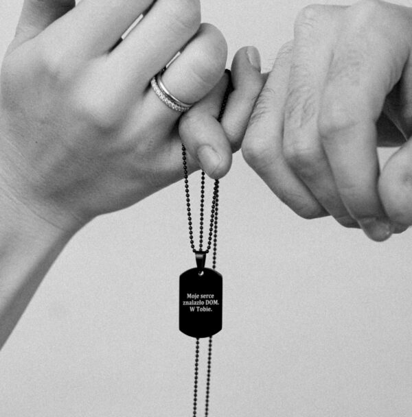 Dwie osoby trzymające wspólnie naszyjnik z napisem 'Moje serce znalazło DOM. W Tobie.'