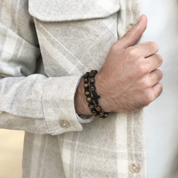 Ręka mężczyzny z bransoletką z drewnianych koralików z krzyżykiem.