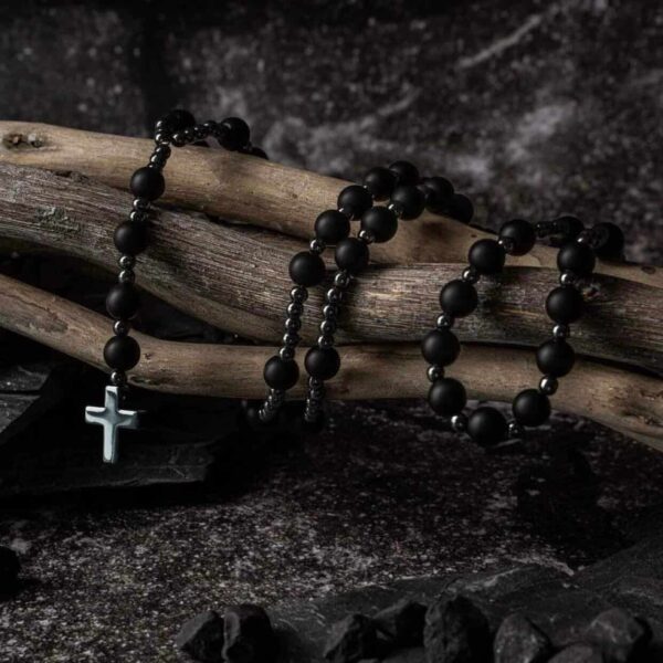 Czarny różaniec z krzyżem na tle drewnianych gałęzi