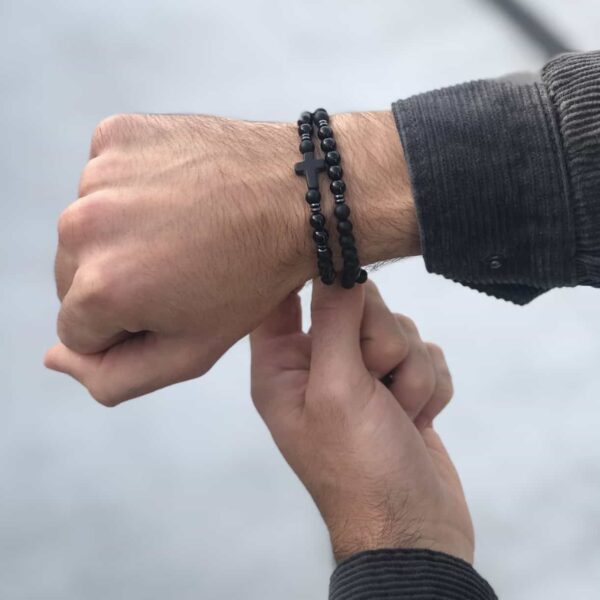 Osoba zakładająca bransoletkę z koralikami i krzyżykiem na nadgarstek.
