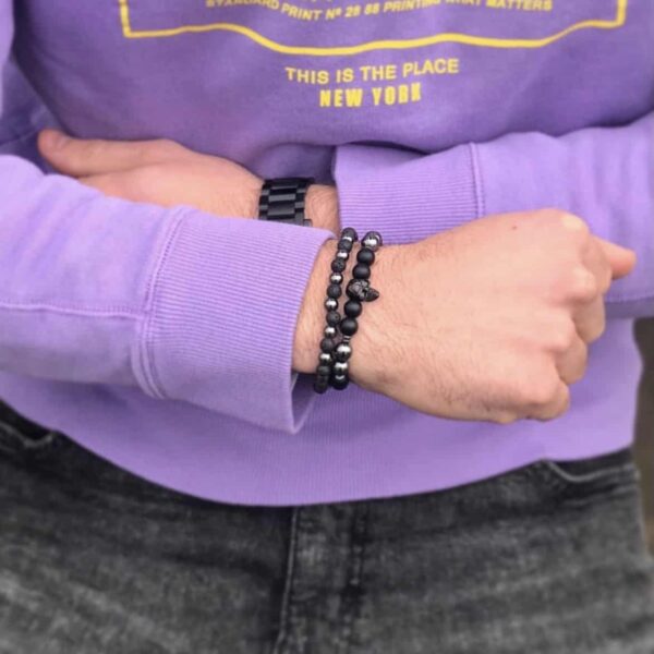 Osoba w fioletowej bluzie z założonymi rękami, na nadgarstku bransoletki z czarnymi koralikami.