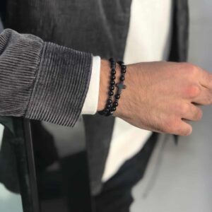 Męska ręka z bransoletką z czarnymi koralikami i krzyżem.