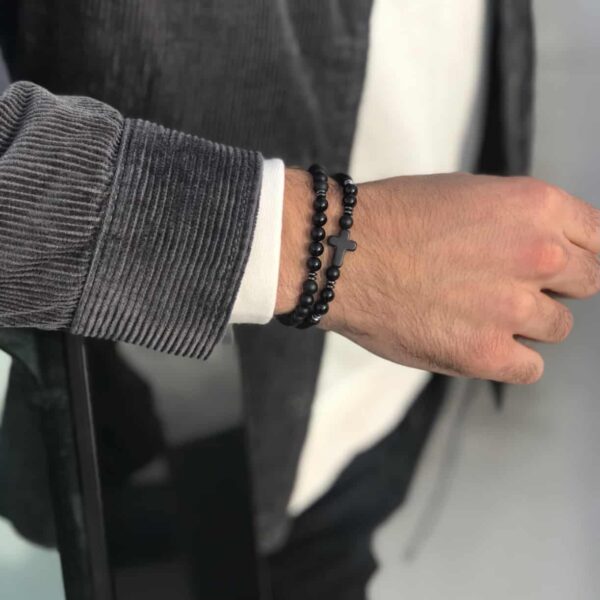 Męska ręka z bransoletką z czarnymi koralikami i krzyżem.