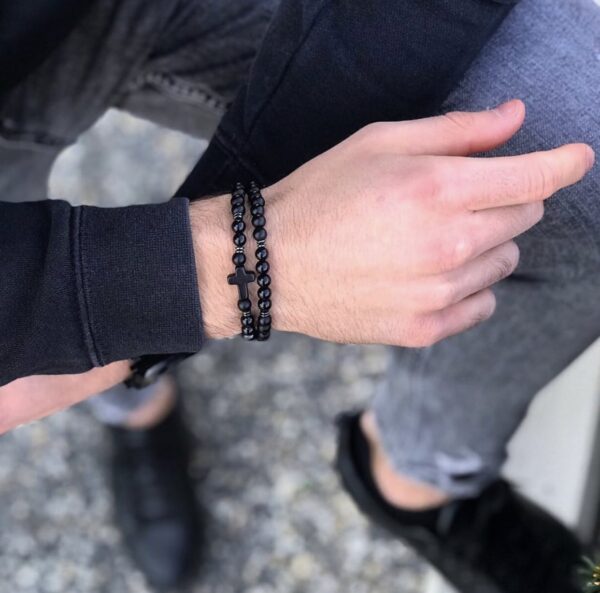 Osoba nosząca czarne koralikowe bransoletki z krzyżem na nadgarstku.