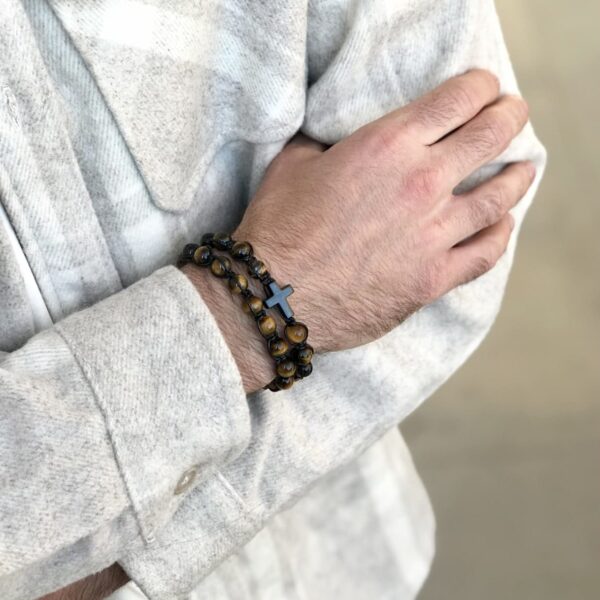 Mężczyzna w jasnej koszuli noszący bransoletkę z krzyżykiem.