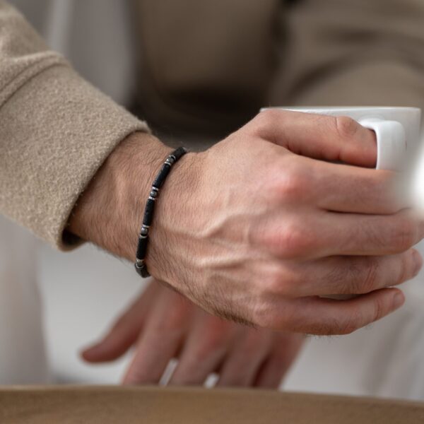 Osoba trzymająca filiżankę kawy z bransoletką na nadgarstku.