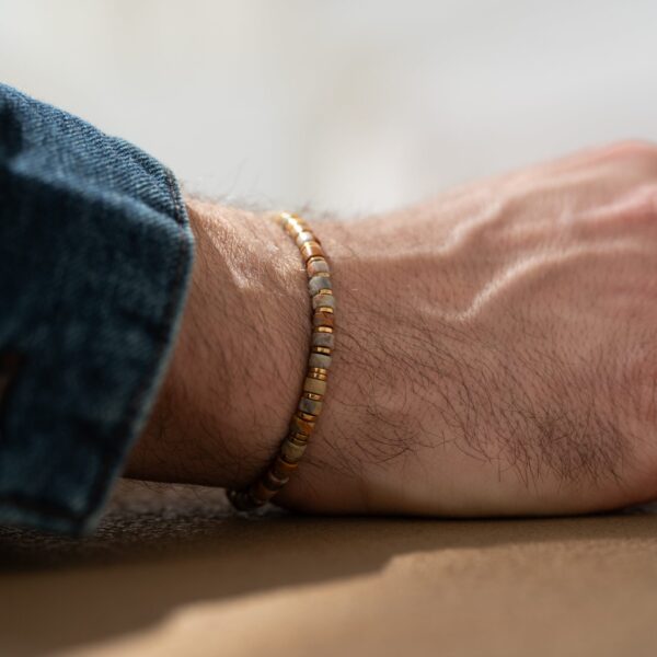 Męska ręka z bransoletką z koralików w różnych odcieniach złota i srebra.