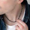 Naszyjnik z kamieniami stylizowany na szyi mężczyzny w białej koszulce i ciemnej kurtce.