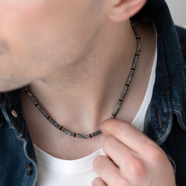 Naszyjnik z kamieniami stylizowany na szyi mężczyzny w białej koszulce i ciemnej kurtce.