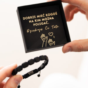 Osoba trzymająca pudełko z napisem 'Dobrze mieć kogoś, na kim można polegać. Dziękuję Ci Tato' oraz czarną bransoletkę.