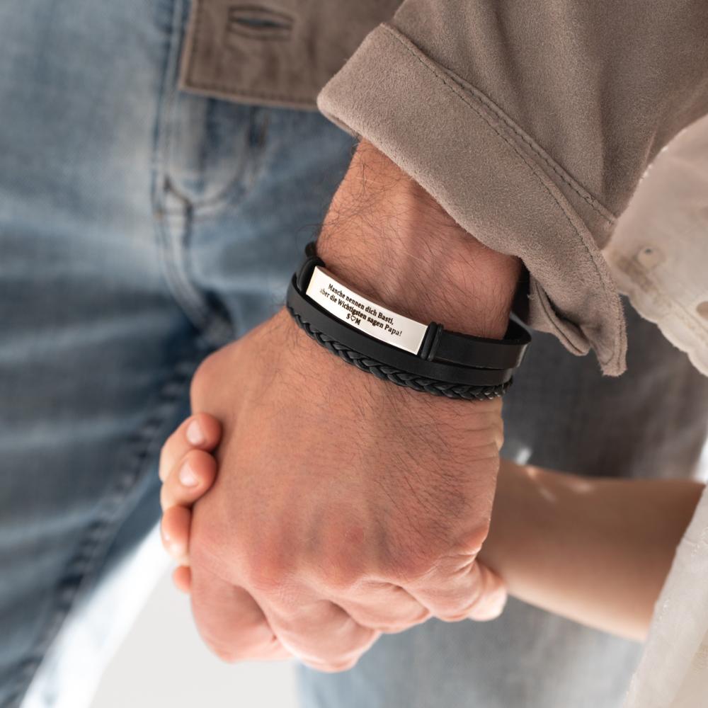 Osoba w szarej koszulce trzymająca za rękę dziecko, na nadgarstku czarny bransoletka z grawerem.