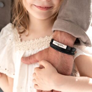 Dziecko trzymające się za rękę z dorosłym noszącym skórzaną bransoletkę.